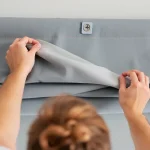 Mężczyzna zdejmujący roletę rzymską do prania; widoczny demontaż materiału z szyny; pranie rolet rzymskich krok po kroku.